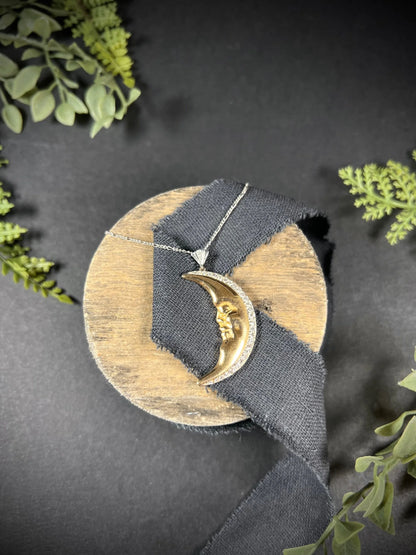 A gold crescent moon pendant with diamonds, with a chain, on a black ribbon
