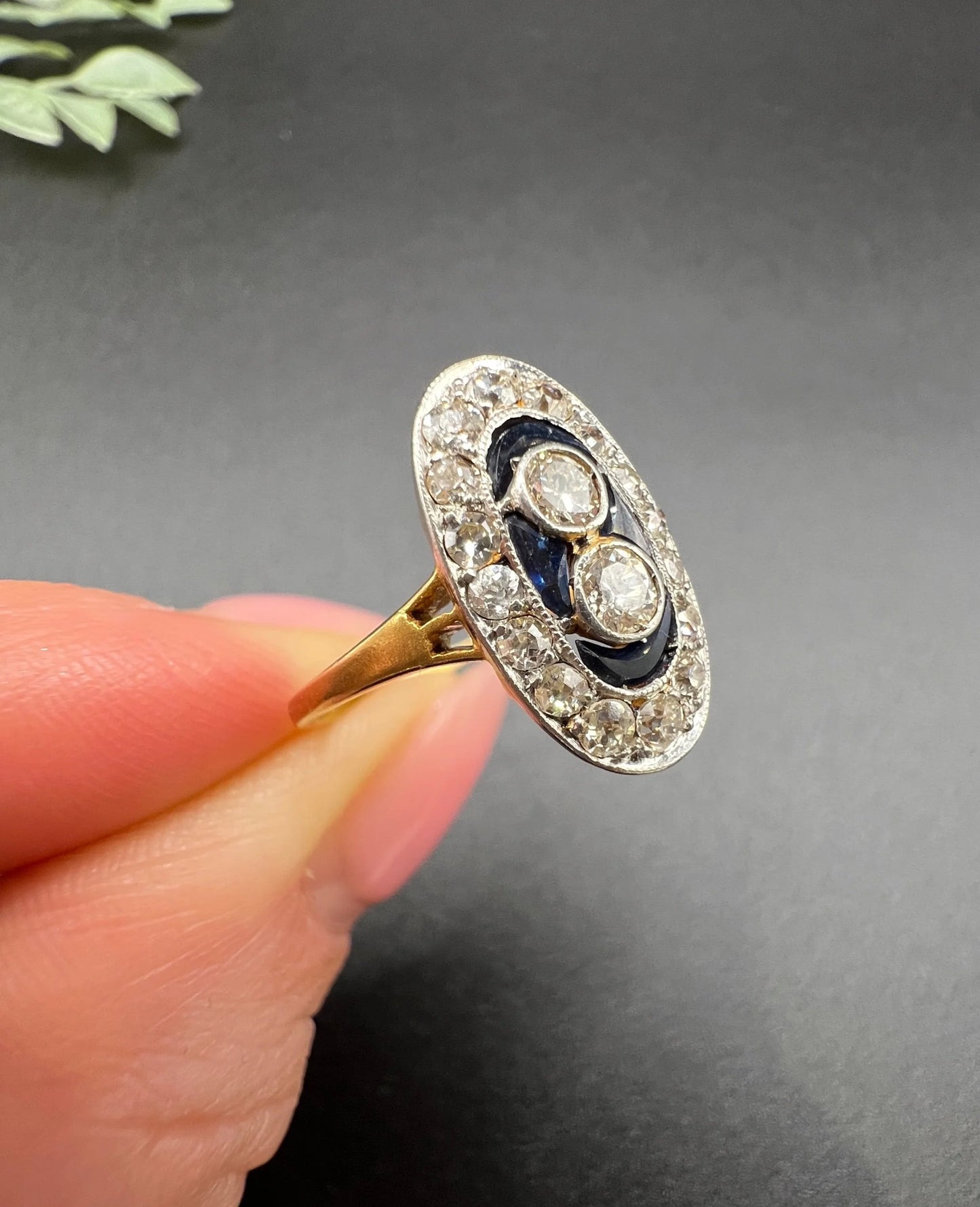 An oval cluster ring with diamonds and sapphires in platinum and yellow gold, held in a hand
