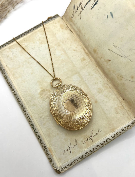 An oval yellow gold locket with intricate engraving, lying on an antique book