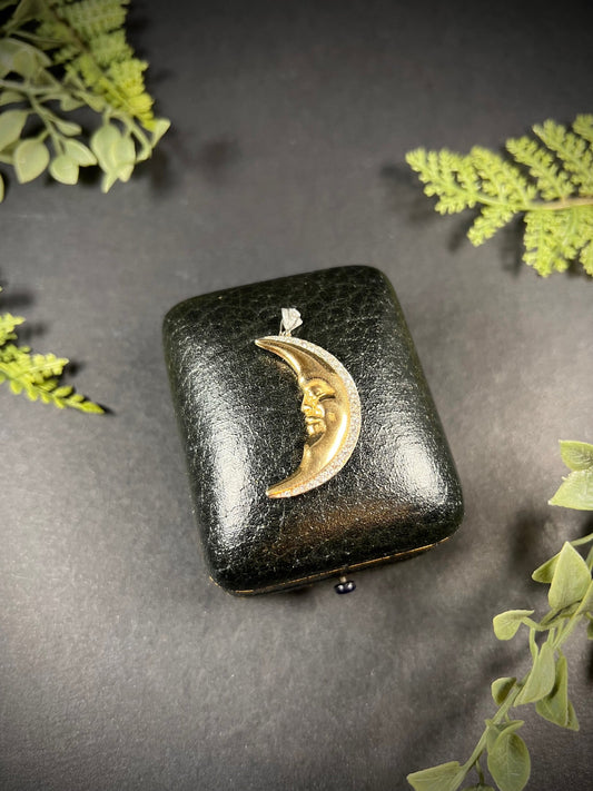 A gold crescent moon pendant with diamonds, on an antique box