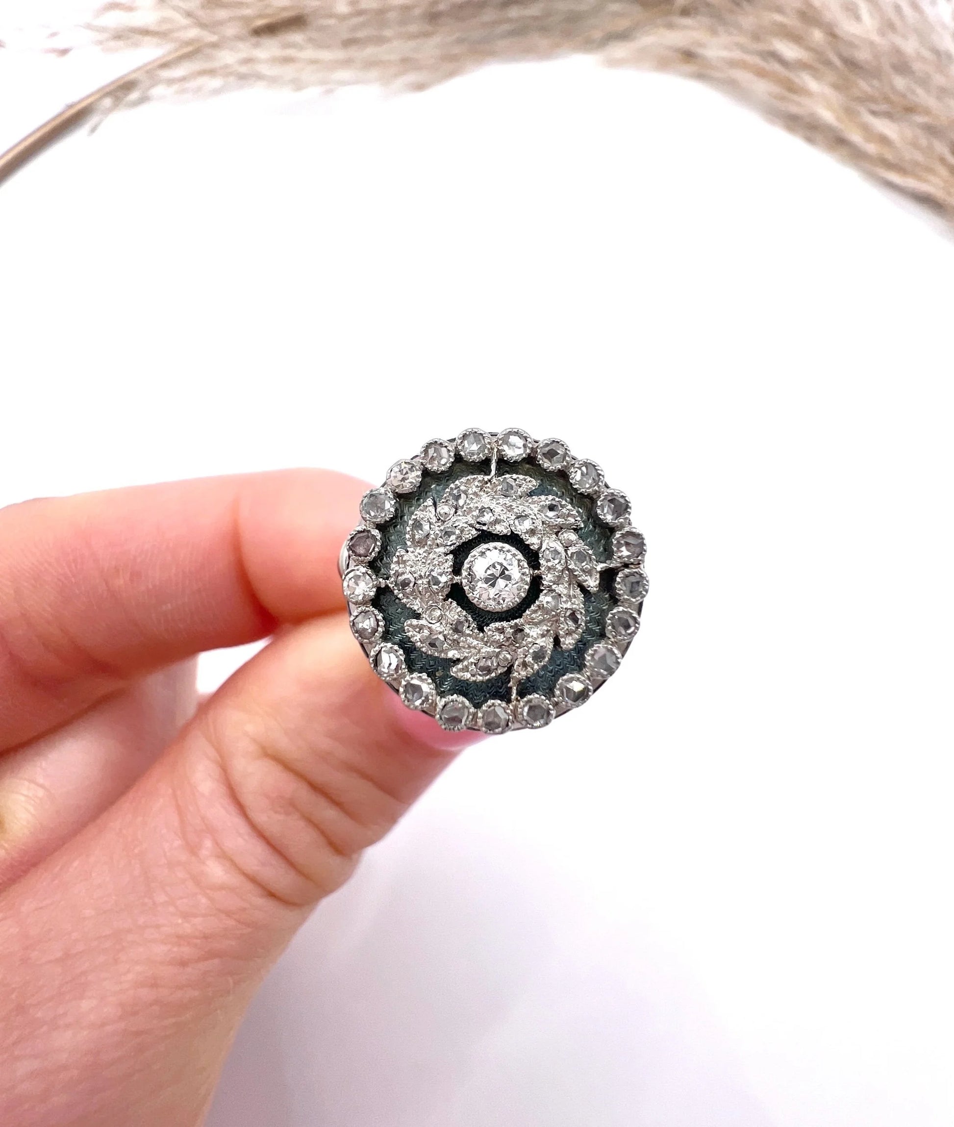 A diamond and dark blue enamel fancy cluster ring in white gold, held in a hand