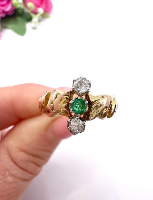 A three stone emerald and diamond ring in yellow and white gold, held in a hand
