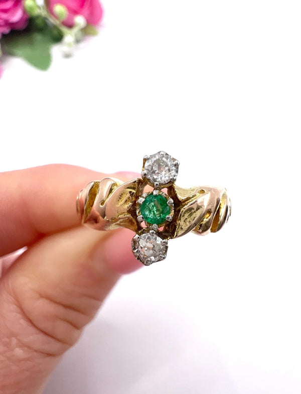 A three stone emerald and diamond ring in yellow and white gold, held in a hand