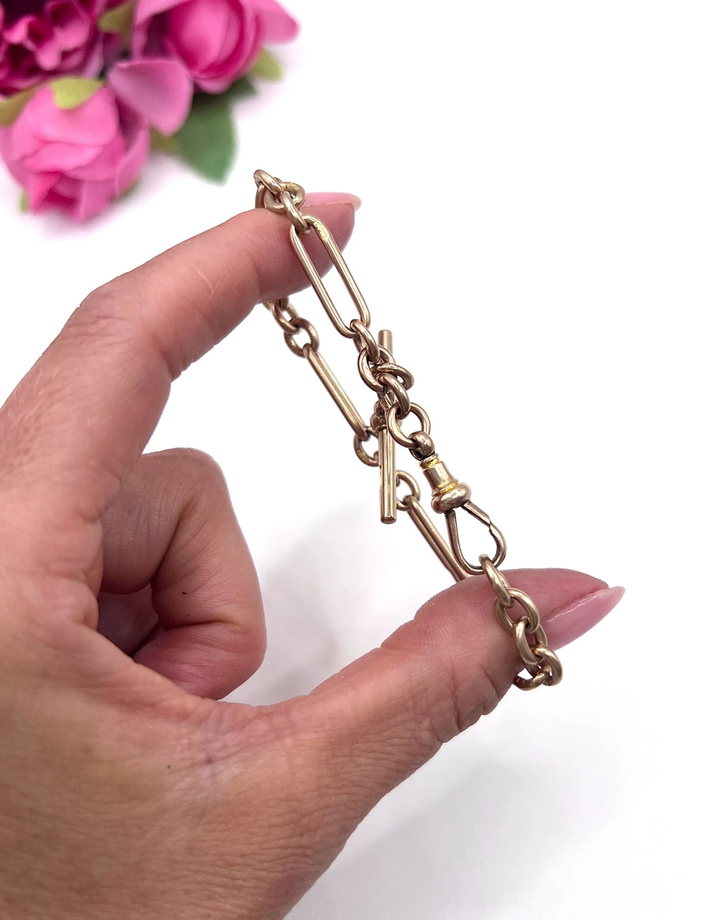 A rose gold link bracelet with a T-bar, held in a hand