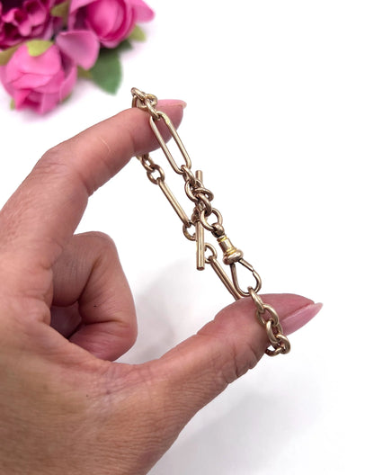 A rose gold link bracelet with a T-bar, held in a hand
