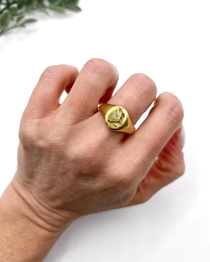 A yellow gold oval signet ring with a seal engraved heraldic crest, modelled on a hand