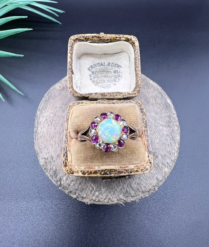 A daisy style cluster ring in rose gold with opal, ruby and diamond, in an antique ring box