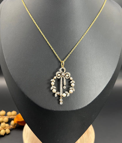 A pearl and diamond bow pendant in gold and platinum, with a chain, on a black bust