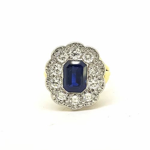 Emerald Cut Sapphire and Diamond Floral Cluster Ring; emerald-cut sapphire surrounded by brilliant-cut diamonds, in white gold to an 18ct yellow gold shank with tri-split shoulders