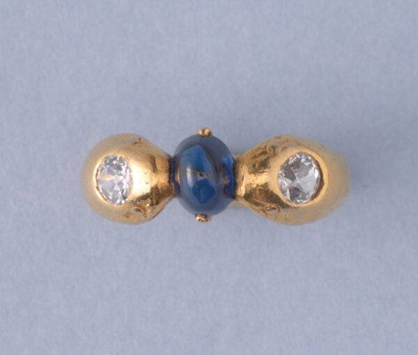Art Deco Sapphire and Old Cut Diamond Snake Ring; two snake heads each set with an old cut diamond and holding a 1.60ct oval cabochon-cut sapphire between them, in platinum with later gilding. France, Circa 1920
