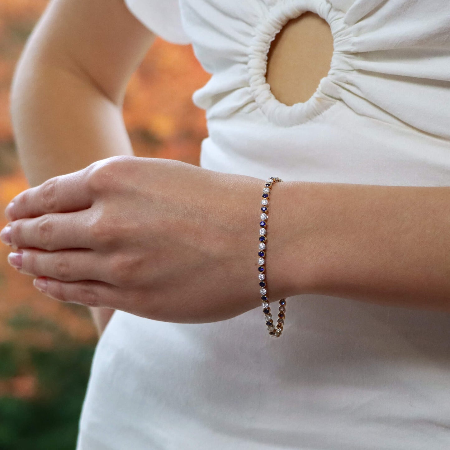 A sapphire and diamond line bracelet in yellow and white gold, modelled on the wrist of a woman wearing a white dress