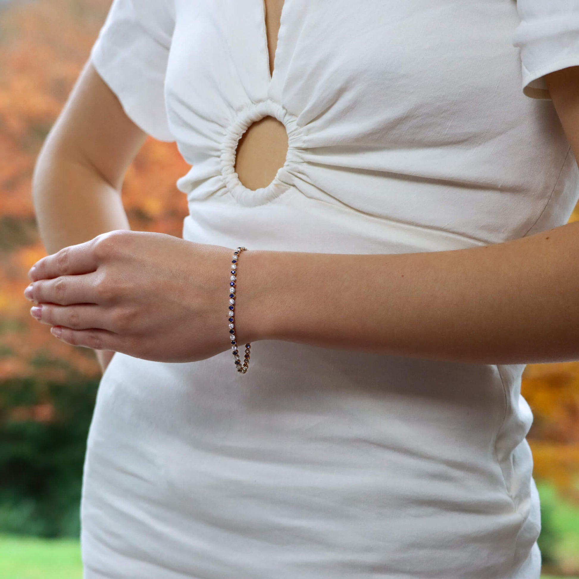 A sapphire and diamond line bracelet in yellow and white gold, modelled on the wrist of a woman wearing a white dress