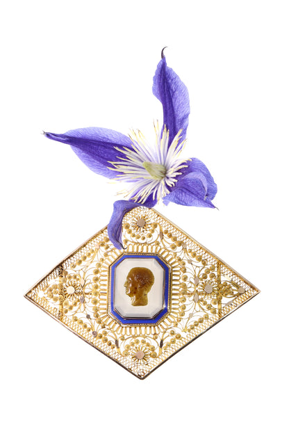A yellow gold ornate openwork brooch with an agate cameo portrait in the centre, bordered with blue enamel, with a purple flower