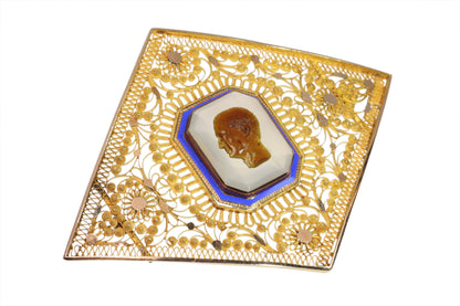 A yellow gold ornate openwork brooch with an agate cameo portrait in the centre, bordered with blue enamel