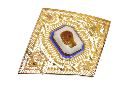 A yellow gold ornate openwork brooch with an agate cameo portrait in the centre, bordered with blue enamel