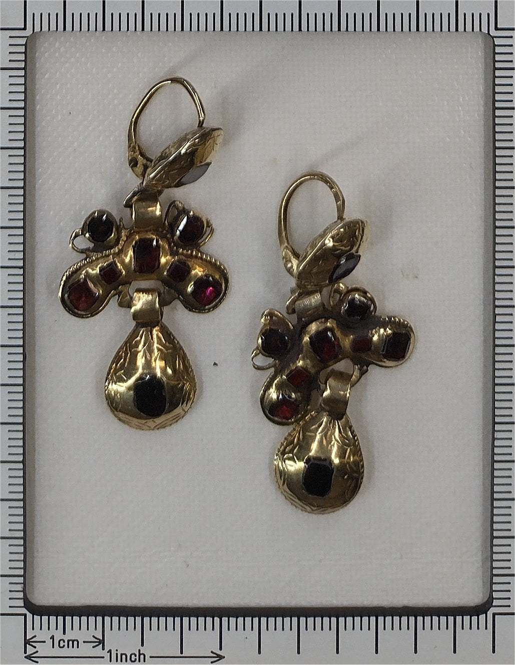A pair of Iberian drop earrings in yellow gold with garnets, next to a ruler