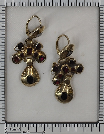A pair of Iberian drop earrings in yellow gold with garnets, next to a ruler