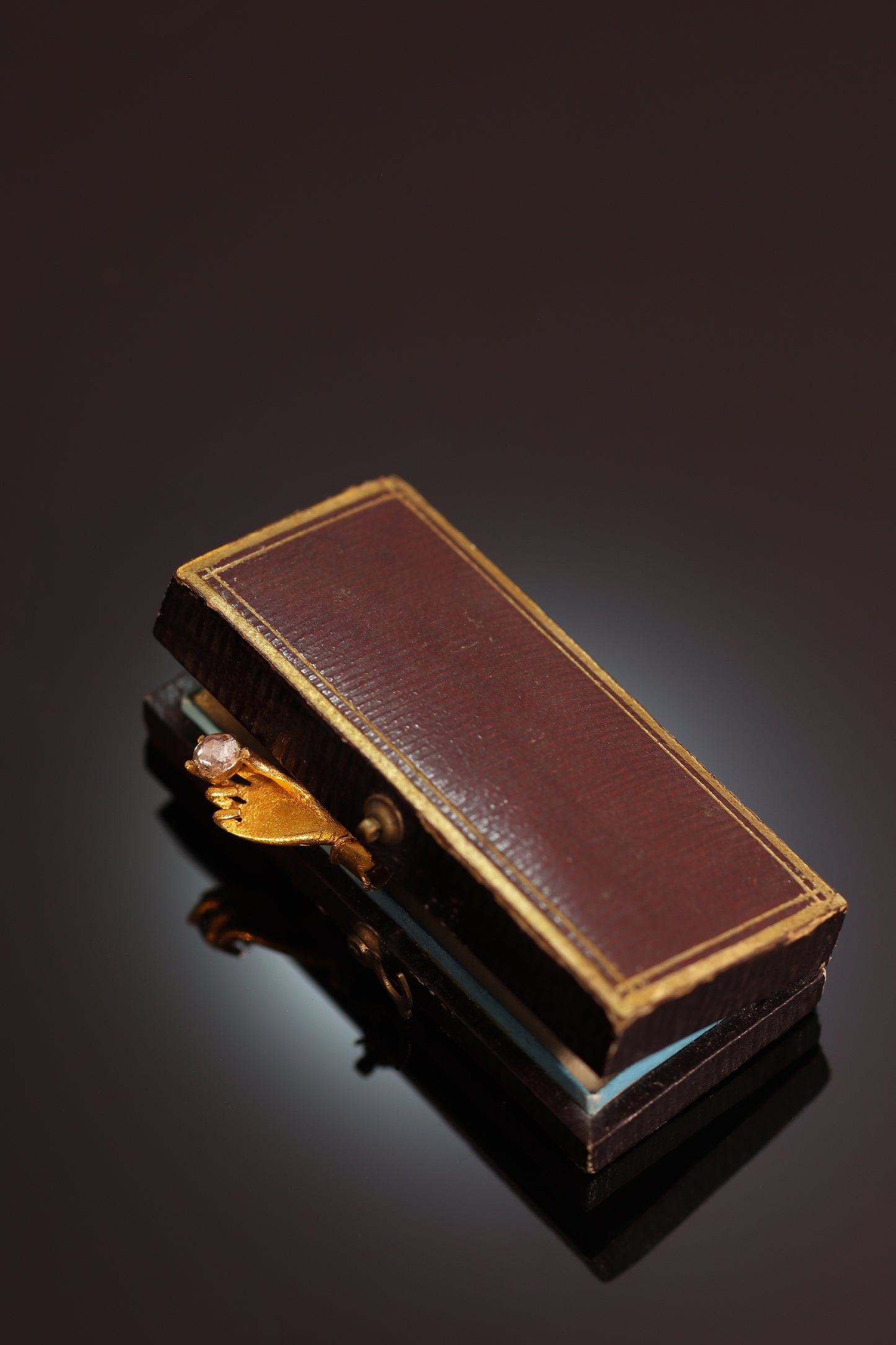 A yellow gold hand holding a diamond stick or tie pin, in an antique box