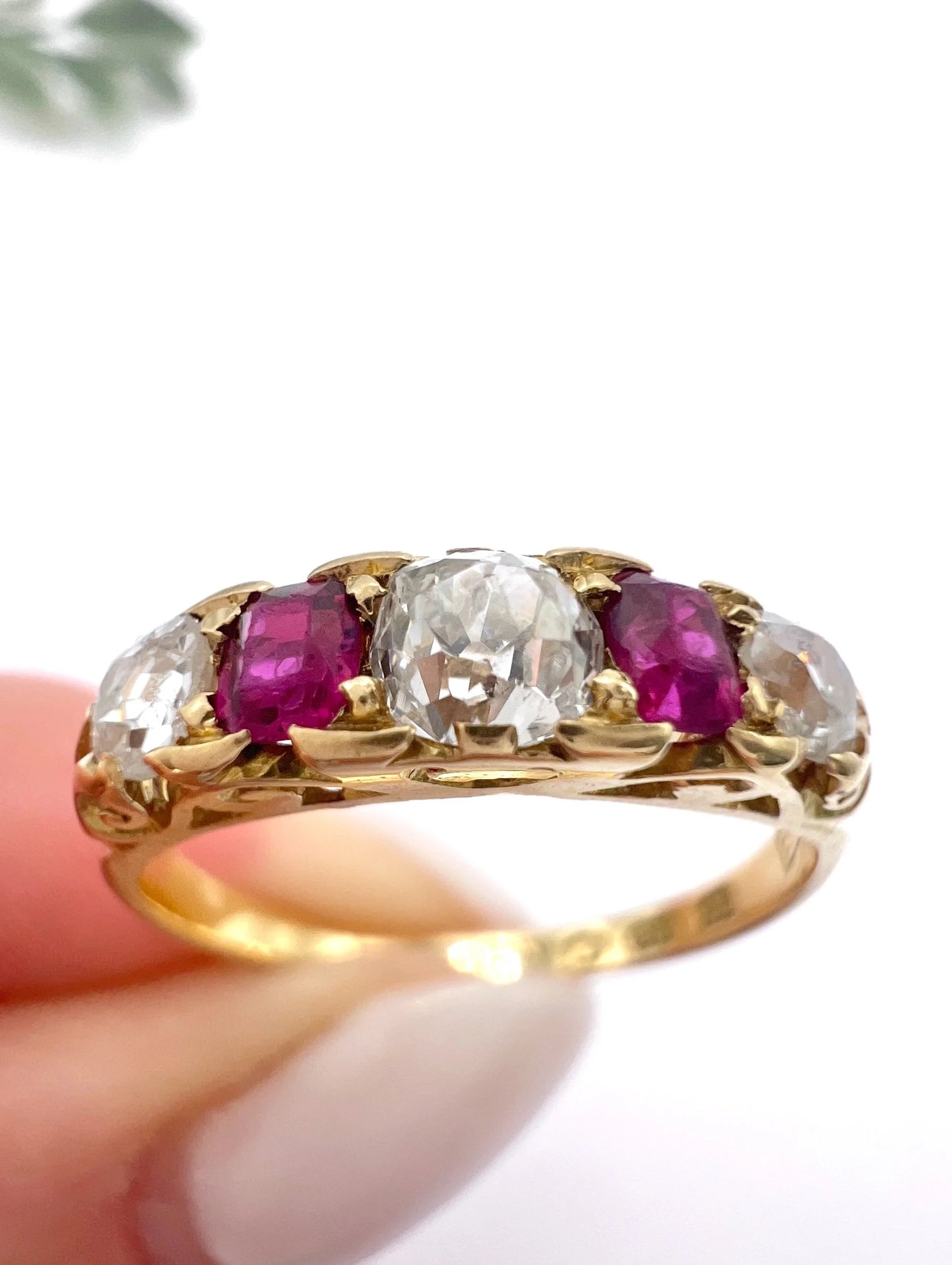 A yellow gold ruby and diamond five stone ring, held in a hand