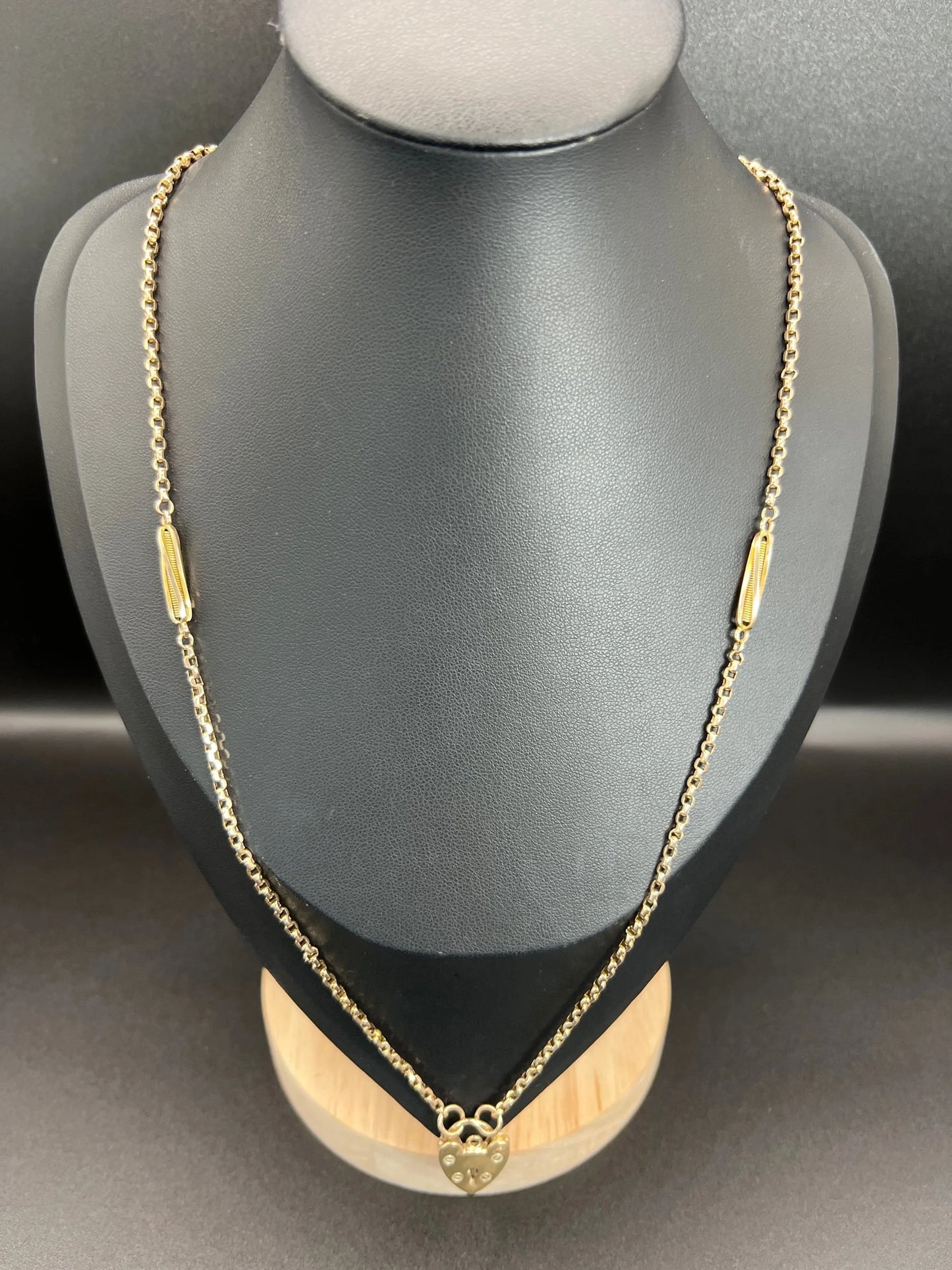A yellow gold fancy link chain with a heart padlock, on a black bust