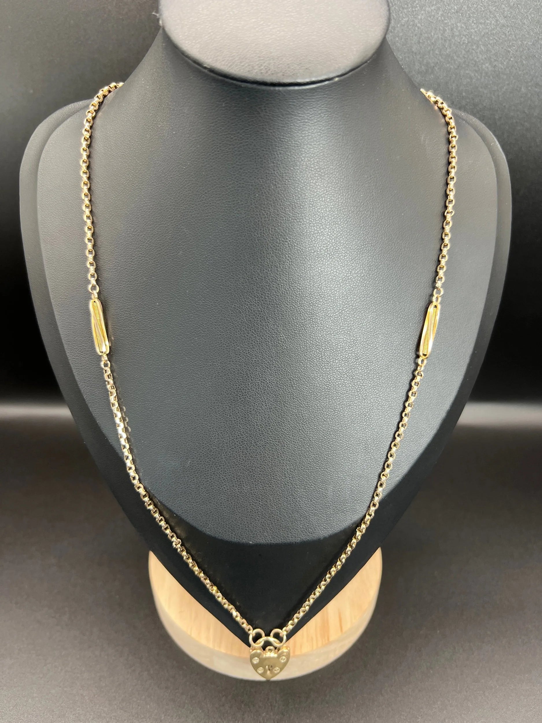 A yellow gold fancy link chain with a heart padlock, on a black bust