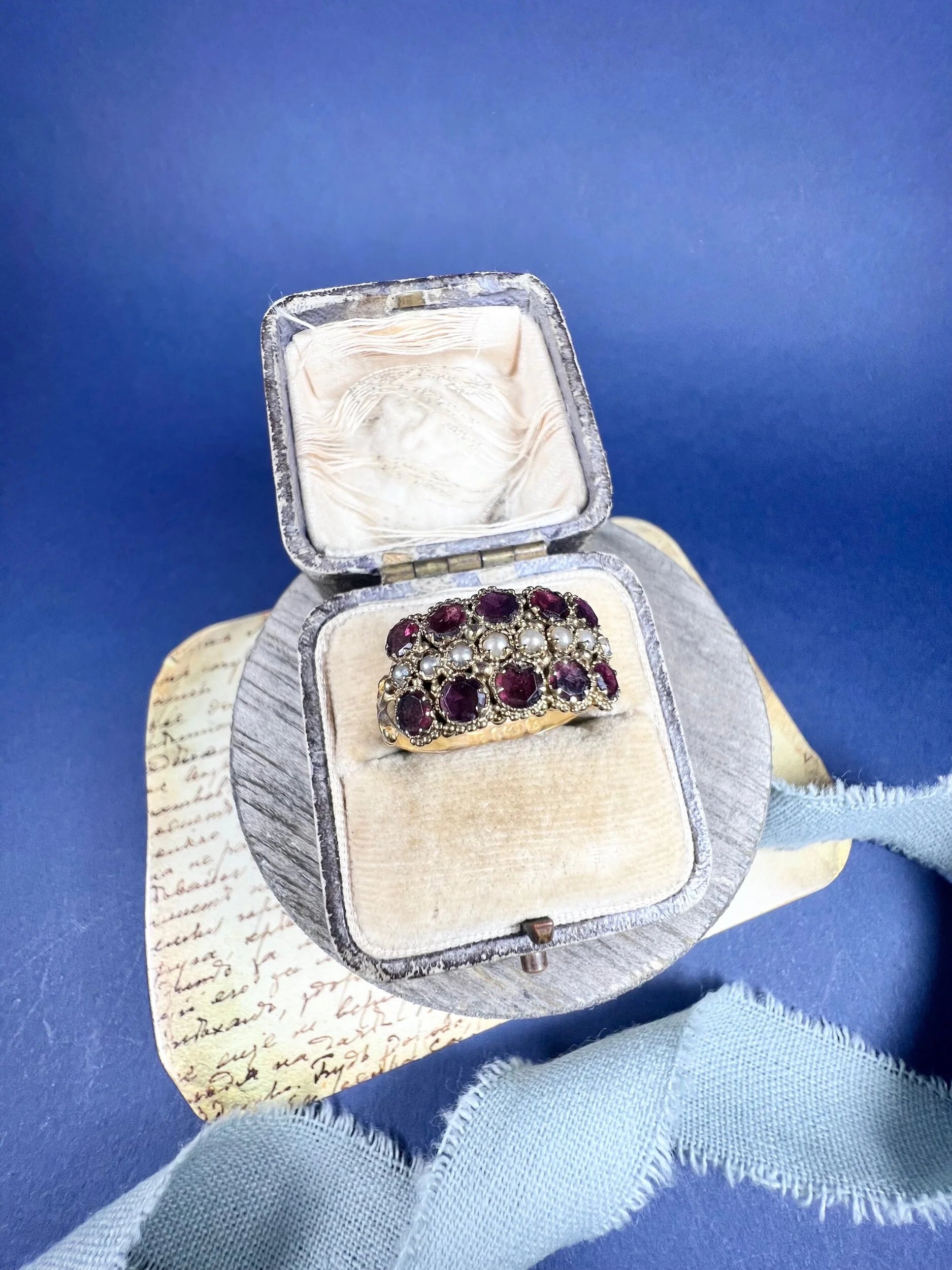 A yellow gold triple row ring with garnets and seed pearls, in a ring box