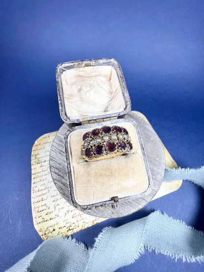 A yellow gold triple row ring with garnets and seed pearls, in a ring box