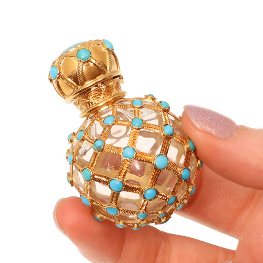 A yellow gold decorative perfume bottle with cabochon turquoise, held in a hand