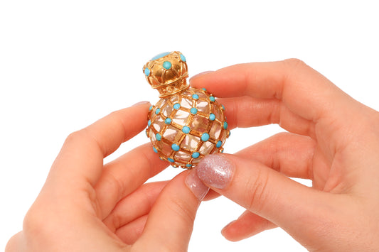A yellow gold decorative perfume bottle with cabochon turquoise, held in hands
