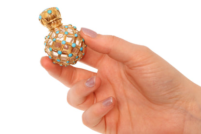 A yellow gold decorative perfume bottle with cabochon turquoise, held in a hand