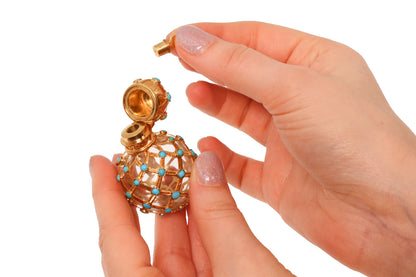 A yellow gold decorative perfume bottle with cabochon turquoise, held in hands