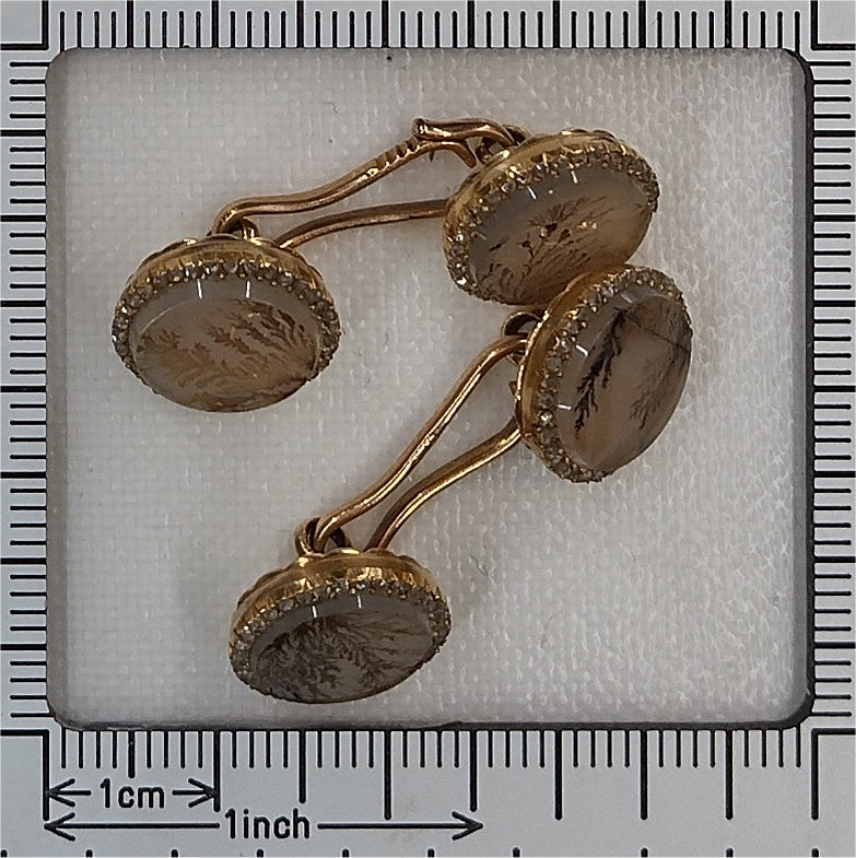 A pair of yellow gold circular cufflinks with moss agate and diamonds, next to a ruler