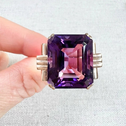 A large single stone amethyst cocktail ring in yellow gold, held in a hand