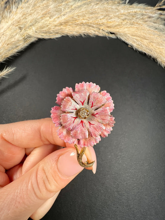 A pink enamelled flower brooch with a diamond centre, in yellow gold, held in a hand