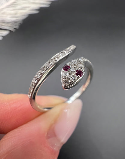 A white gold snake ring set with diamonds and with ruby eyes, held in a hand