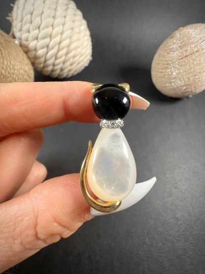 A cat-shaped brooch in yellow gold with black onyx, mother of pearl and a diamond set collar, held in a hand