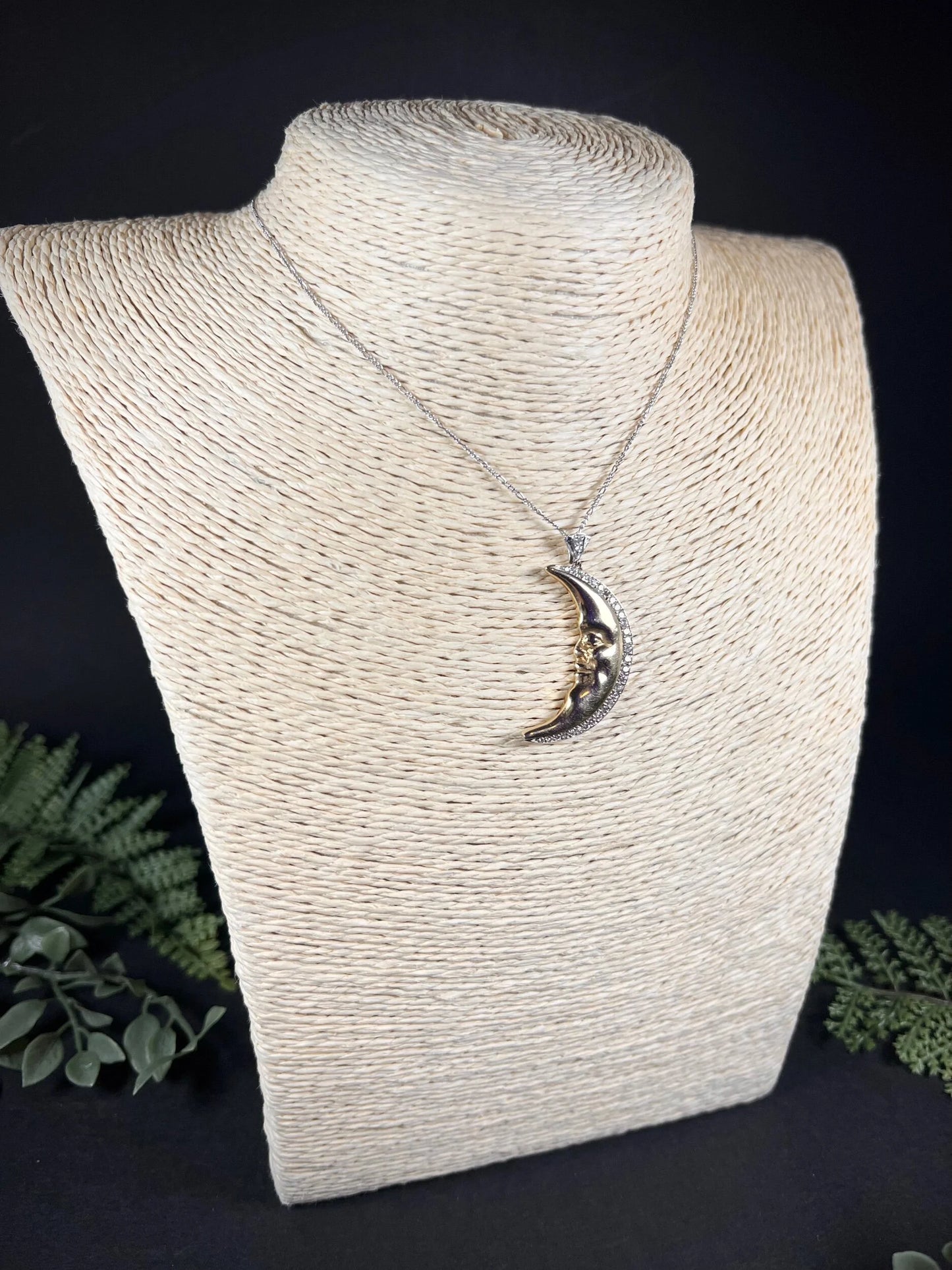 A gold crescent moon pendant with diamonds, on a chain, modelled on a jewellery bust