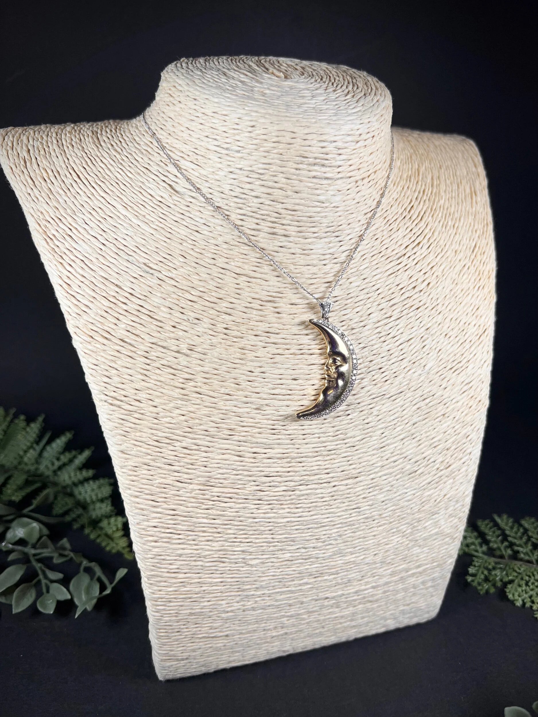 A gold crescent moon pendant with diamonds, on a chain, modelled on a jewellery bust