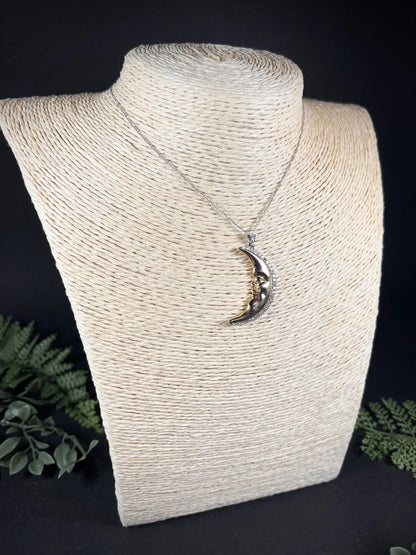 A gold crescent moon pendant with diamonds, on a chain, modelled on a jewellery bust