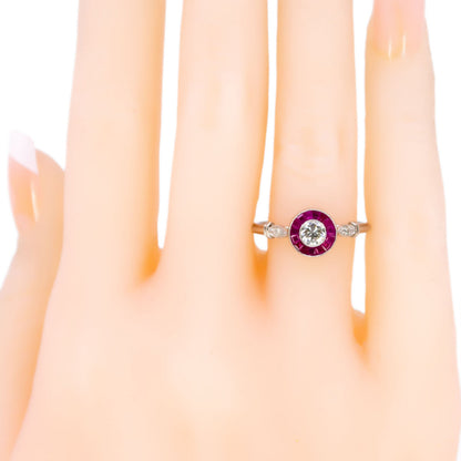 A brilliant cut diamond and french cut ruby halo target cluster ring in platinum, modelled on a hand
