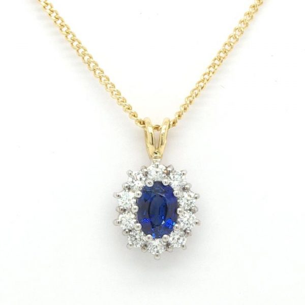 Sapphire and Diamond Oval Cluster Pendant; 0.50 carat oval faceted sapphire surrounded by 1.04 carats of round brilliant-cut diamonds in 18ct white gold. Hung from an 18ct yellow gold bale to an 18ct yellow gold 18-inch curb chain