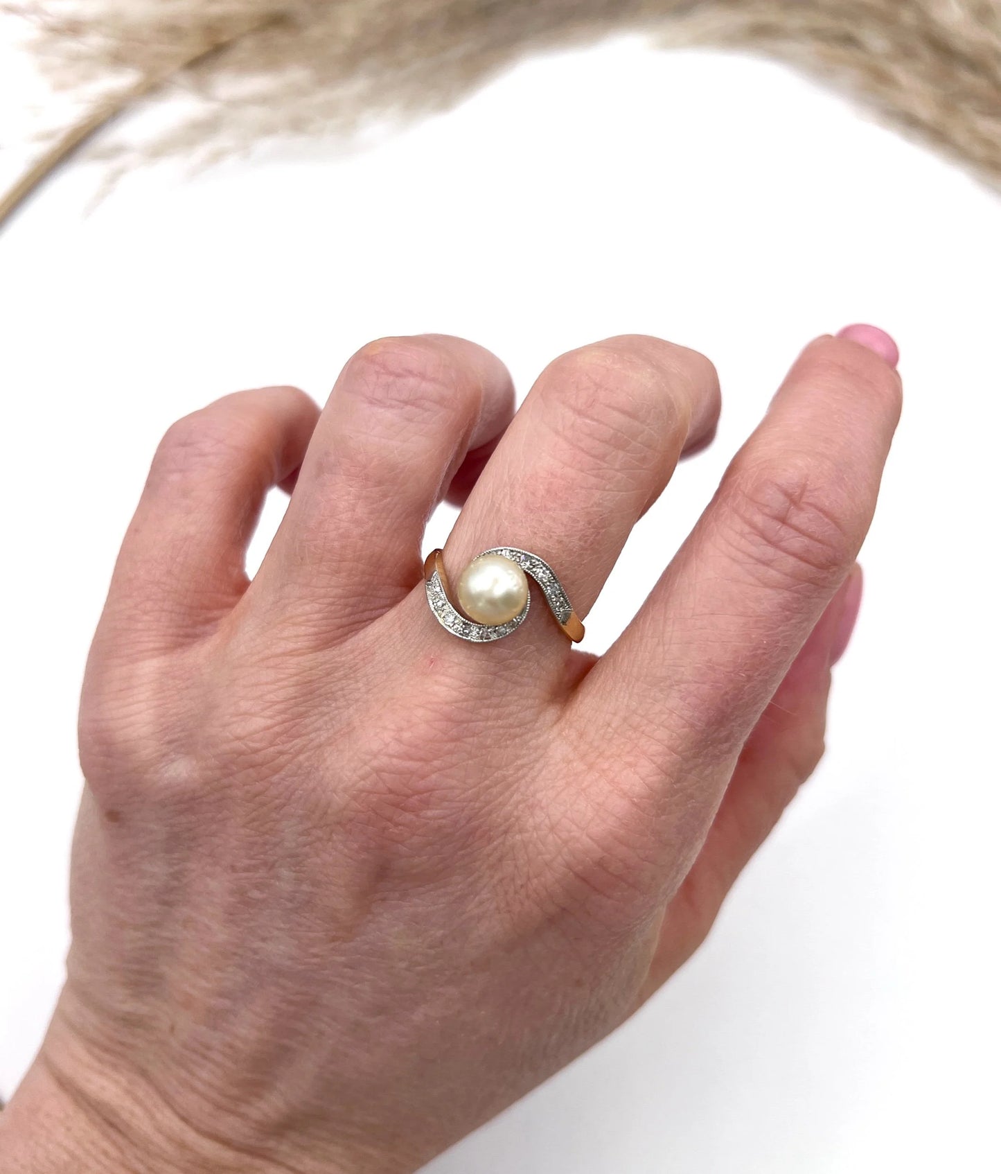 A pearl and diamond crossover swirl ring in yellow and white gold, modelled on a hand