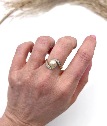 A pearl and diamond crossover swirl ring in yellow and white gold, modelled on a hand