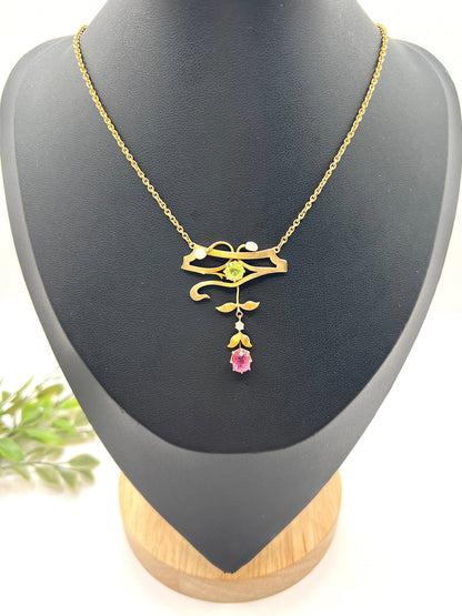 A yellow gold pendant necklace with pearls, a peridot, a diamond and a pink tourmaline drop, on a black jewellery bust