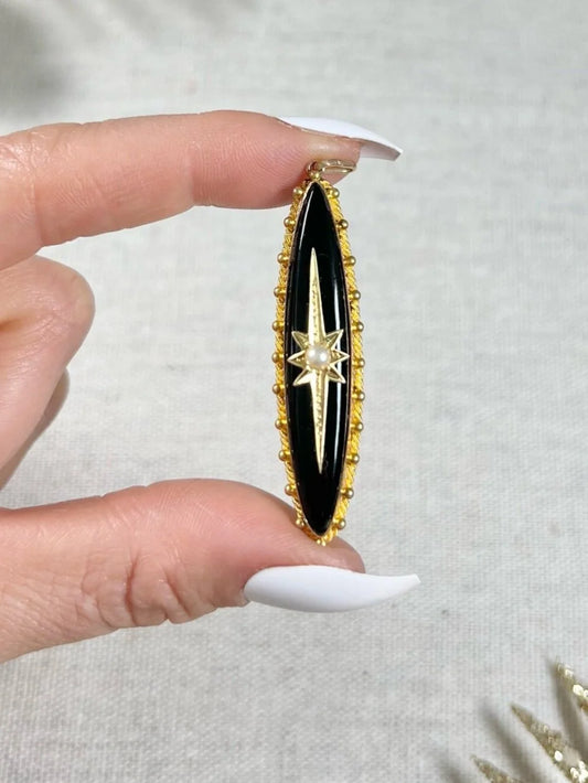 An elongated yellow gold pendant with black onyx and a pearl centre