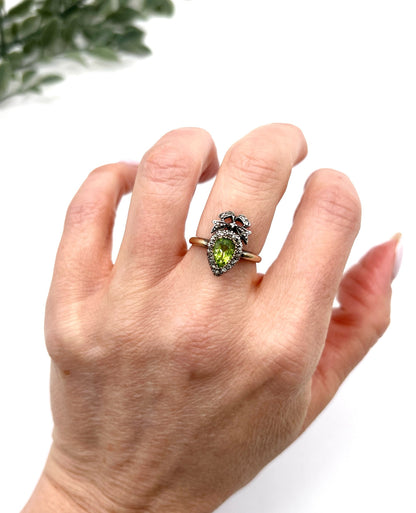 A pear cut peridot and round diamond cluster ring with bow detail, in yellow gold and white metal, modelled on a hand