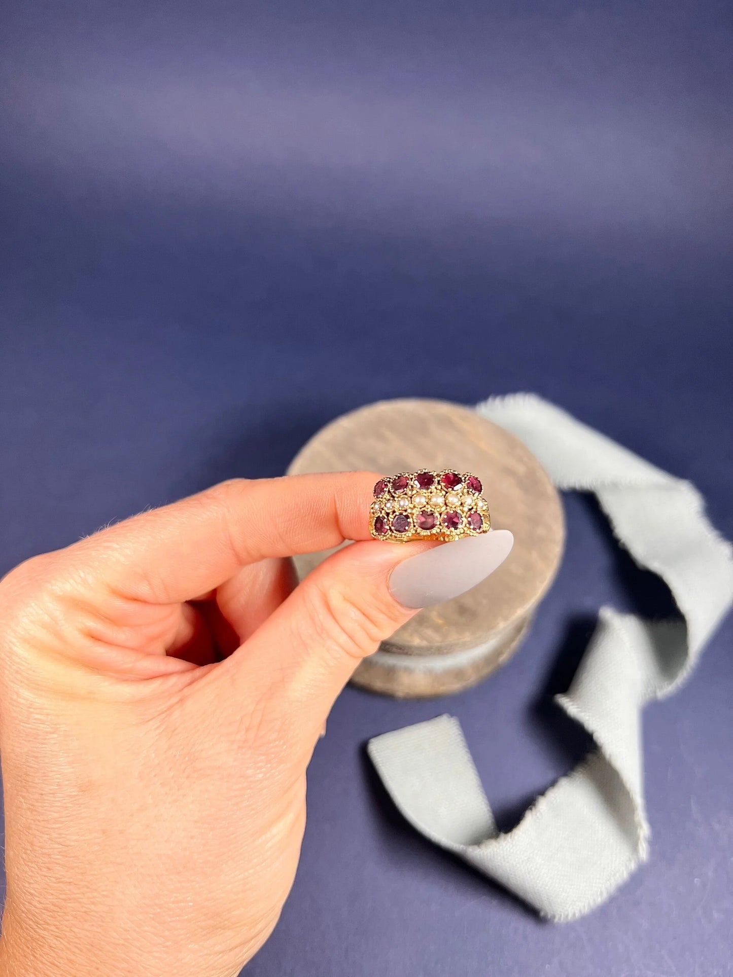A yellow gold triple row ring with garnets and seed pearls, held in a hand