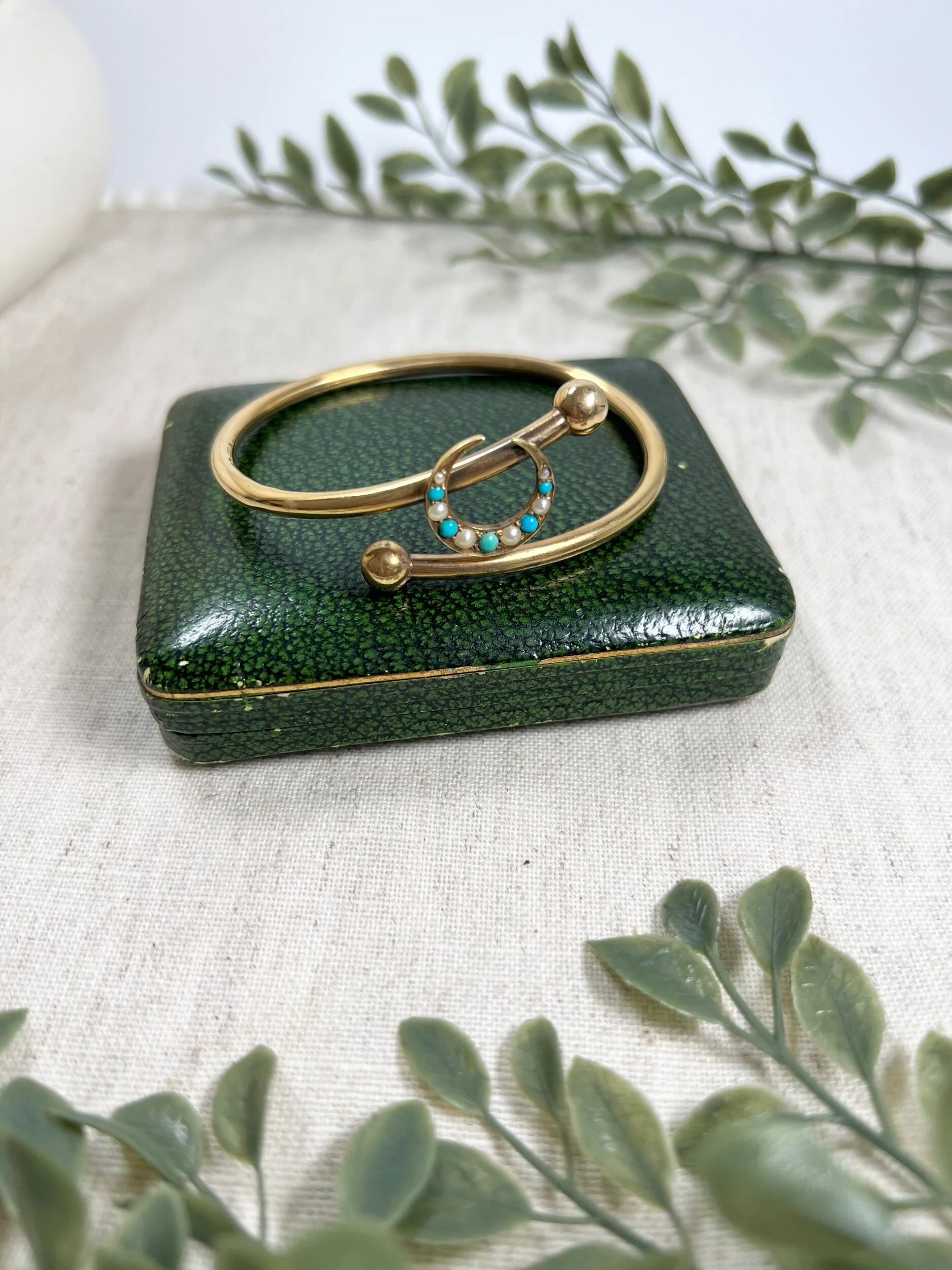 A yellow gold crossover bangle bracelet with a pearl and turquoise crescent moon centre