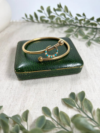 A yellow gold crossover bangle bracelet with a pearl and turquoise crescent moon centre