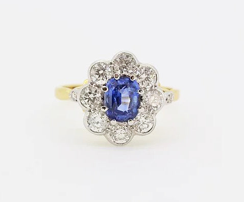 Sapphire and Diamond Floral Cluster Ring; central 1.60ct oval sapphire surrounded by 1.25cts diamonds, diamond set shoulders, 18ct yellow gold shank